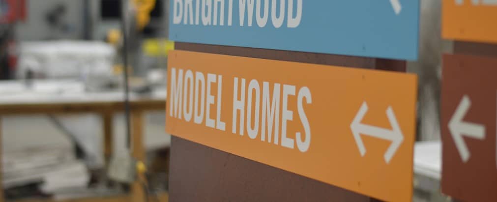 Directional sign on post in warehouse, reads "model homes" with arrows